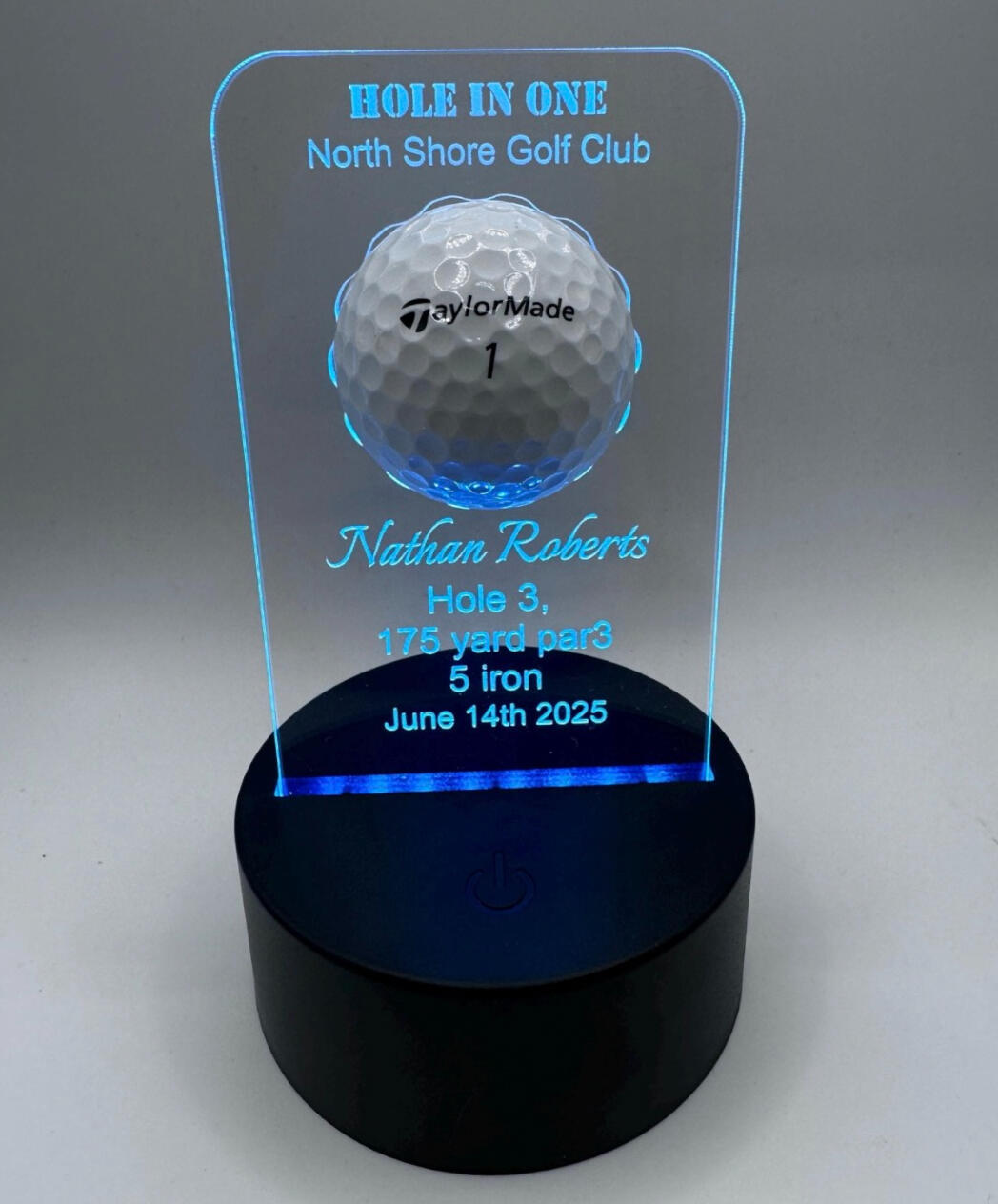 Personalised illuminated acrylic hole-in-one golf ball display plaque featuring a golf course background, club name, and player details.