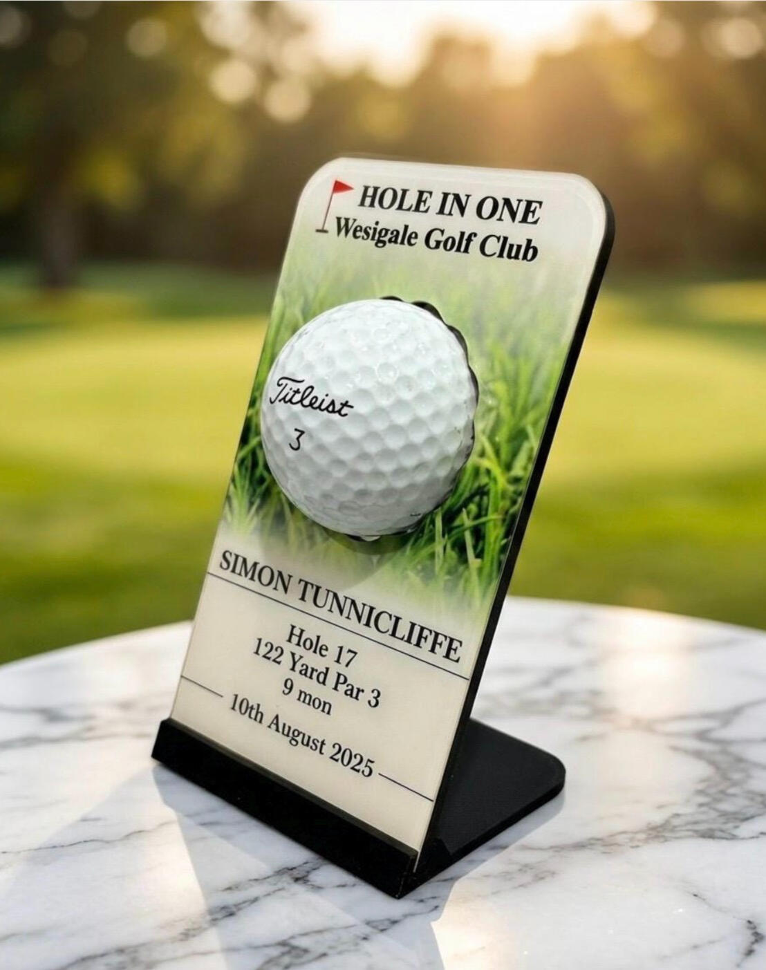 Personalised acrylic hole-in-one golf ball display plaque featuring a golf course background, club name, and player details.